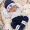 Sesión newborn con conjunto Converse para bebé azul marino Bebé recién nacido durmiendo en cesta de mimbre con conjunto Converse azul marino de gorro y patucos para 0 a 6 meses.