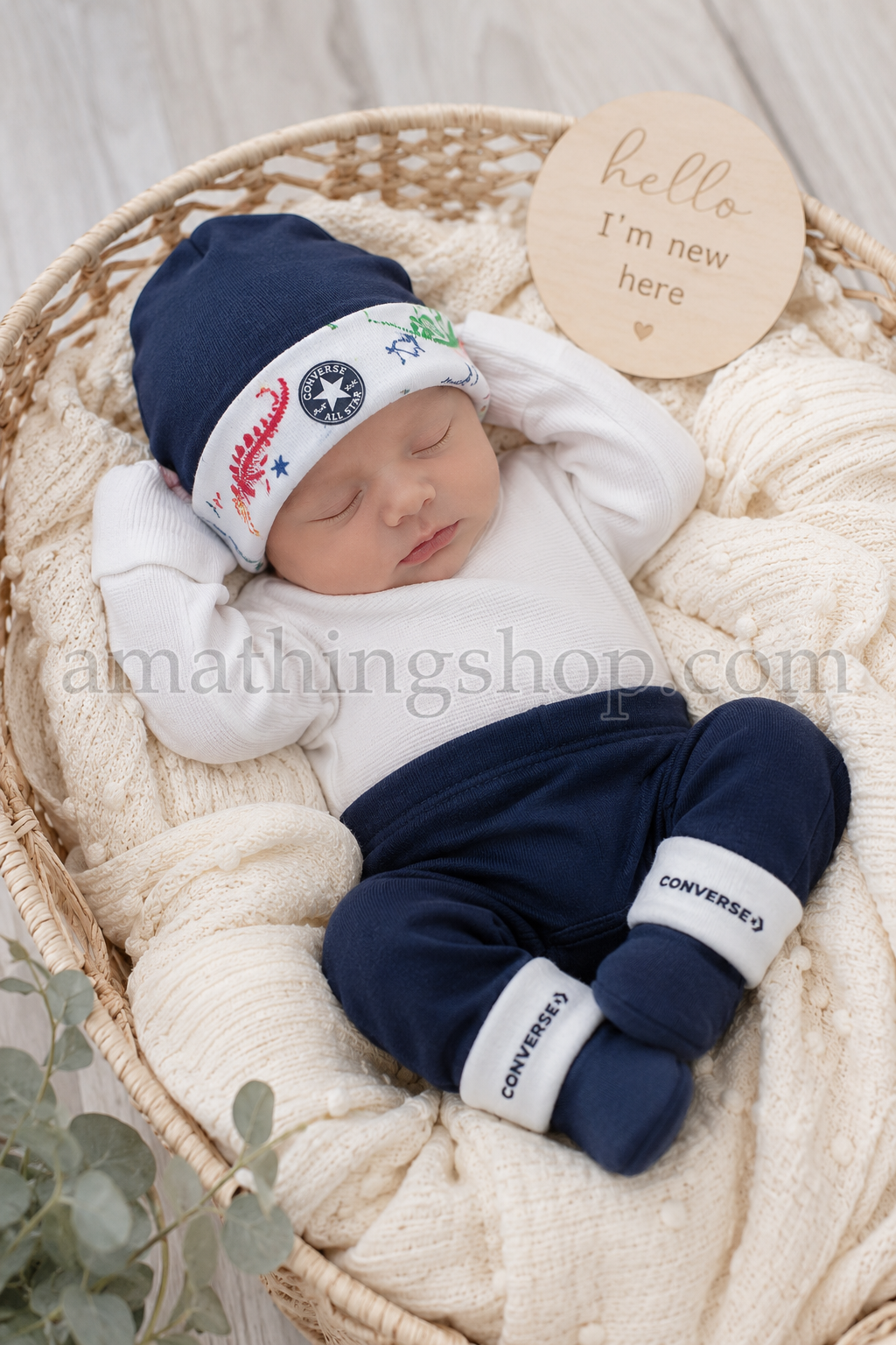 Sesión newborn con conjunto Converse para bebé azul marino Bebé recién nacido durmiendo en cesta de mimbre con conjunto Converse azul marino de gorro y patucos para 0 a 6 meses.