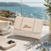 Monedero cartera GUESS original para mujer en color beige crema sobre una mesa con café y vistas al mar