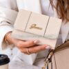 Mujer sujetando un monedero cartera GUESS original color beige crema con logotipo dorado