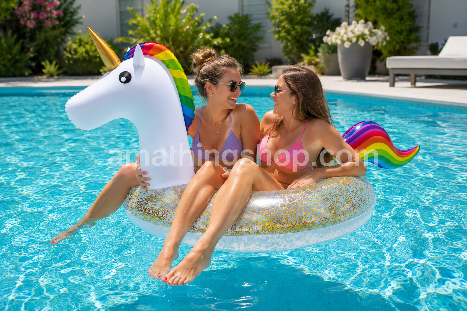 Dos jóvenes disfrutando de un flotador unicornio blanco con purpurina dorada, cuerno dorado y melena arcoíris en una piscina durante un día soleado de verano.