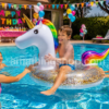 Niños disfrutando de una fiesta de cumpleaños en una piscina con un flotador unicornio blanco con purpurina dorada, melena arcoíris y cuerno dorado durante el verano.