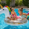 Dos niñas jugando en una piscina con un flotador unicornio blanco con purpurina dorada, cuerno dorado y melena arcoíris durante un día soleado de verano.