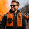 Aficionado Luciendo la Bufanda Oficial Adidas Países Bajos Holanda FJ0994 Oranje Hombre con bufanda oficial Adidas Países Bajos Holanda FJ0994 naranja y negra durante una celebración de aficionados al fútbol con el león de la Oranje y diseño HOLLAND