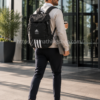 Hombre profesional llevando la mochila Adidas 4ATHLTS Camper Negra HC7269 con portátil en la mano mientras se dirige a la oficina.