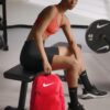 Mujer deportista con mochila Nike Brasilia 9.5 roja en gimnasio