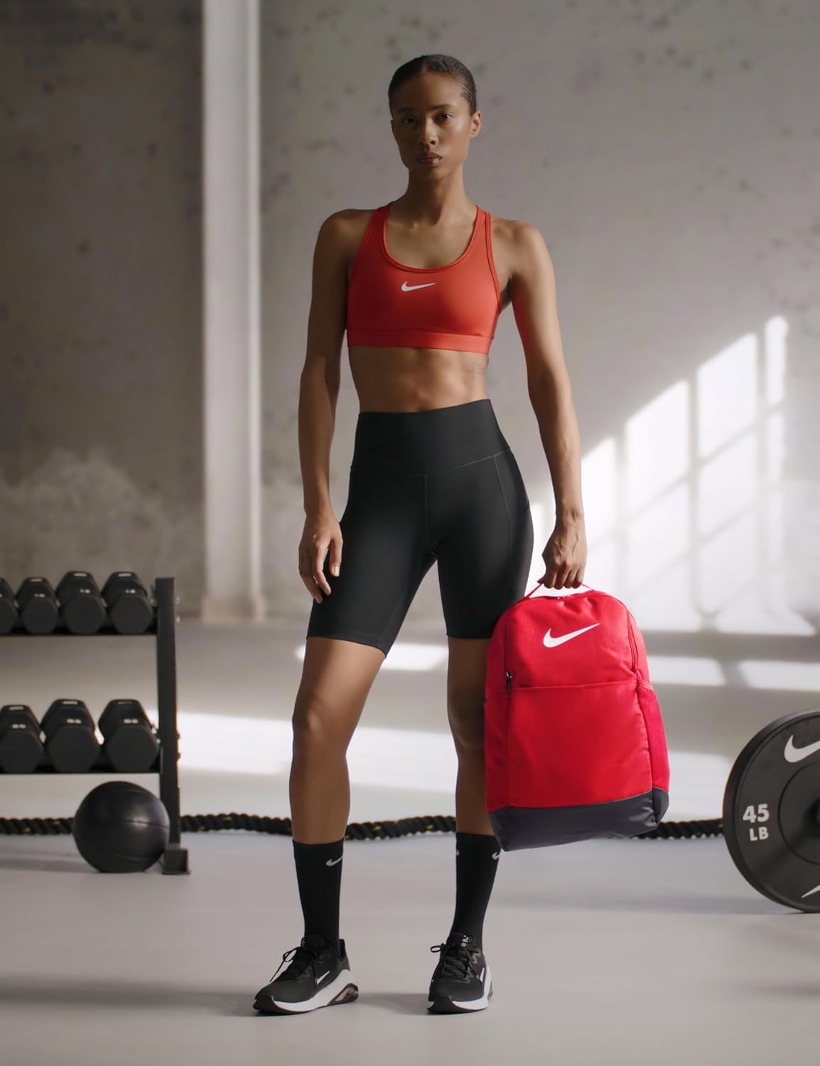 Mochila de entrenamiento Nike Brasilia 9.5 24L roja junto a deportista