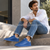 Hombre de unos 35 años sentado en unas escaleras con zapatillas Adidas Stan Smith Recon azules H06186, vaqueros y camisa blanca.