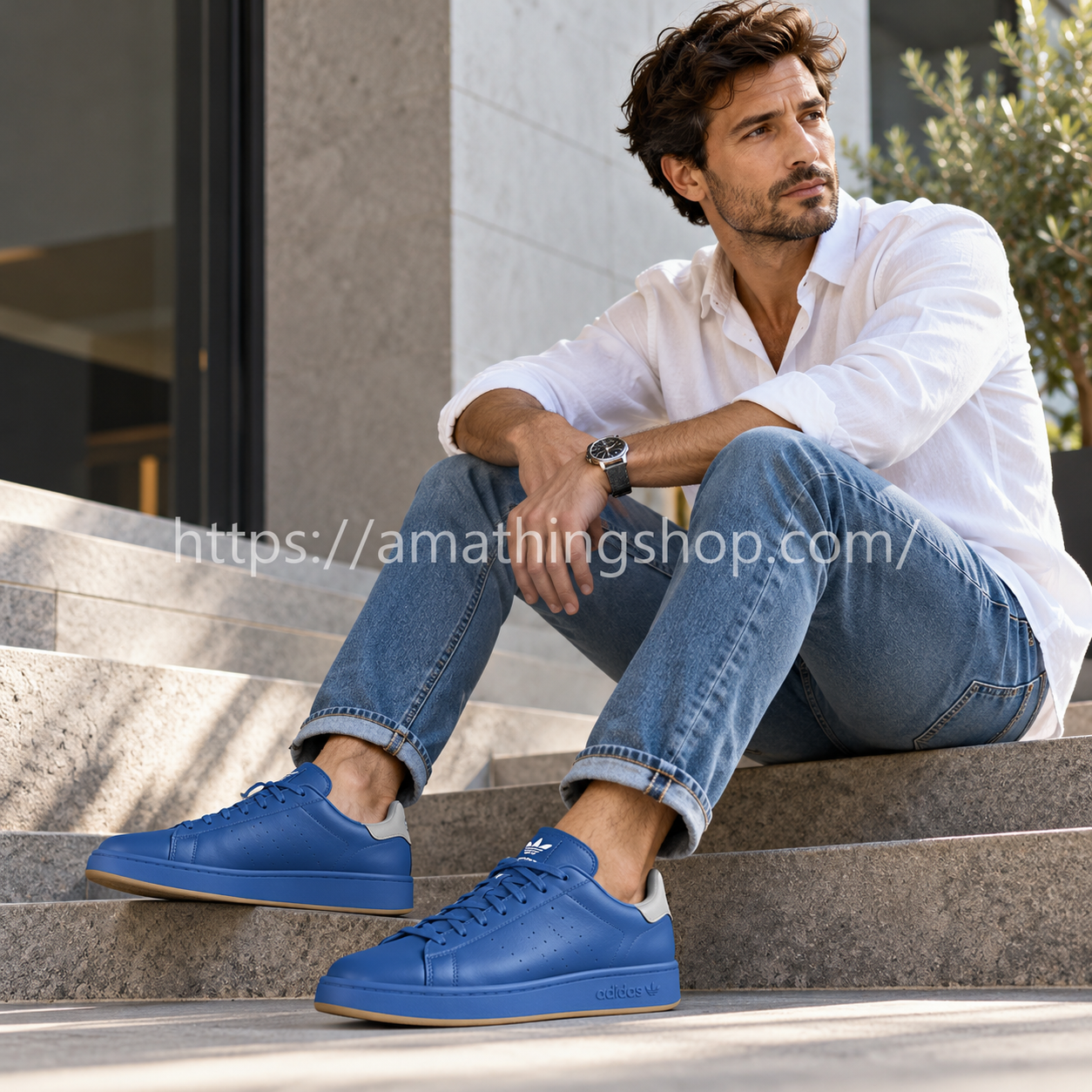 Hombre de unos 35 años sentado en unas escaleras con zapatillas Adidas Stan Smith Recon azules H06186, vaqueros y camisa blanca.