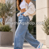 Mujer caminando con zapatillas blancas estilo Jordan Stadium 90, Swoosh azul y detalles rojos, combinadas con vaqueros anchos en un look urbano.