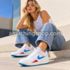 Mujer con vaqueros azules y zapatillas Jordan Stadium 90 blancas, con Swoosh azul y detalles rojos, en un look casual urbano.